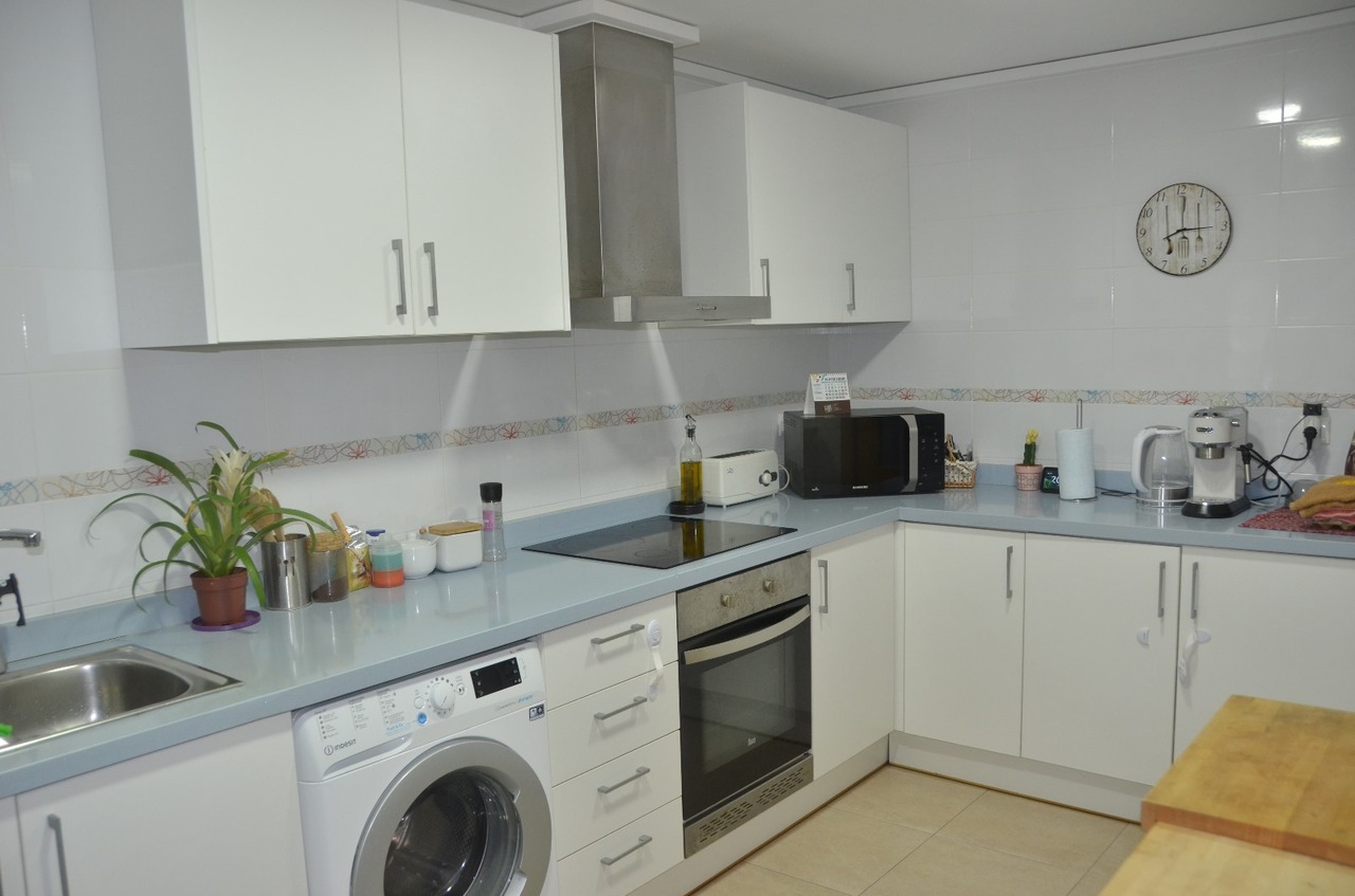 Cuisine équipée de meubles blancs, d'un plan de travail bleu clair, d'un lave-linge intégré, d'un four et d'une plaque de cuisson.