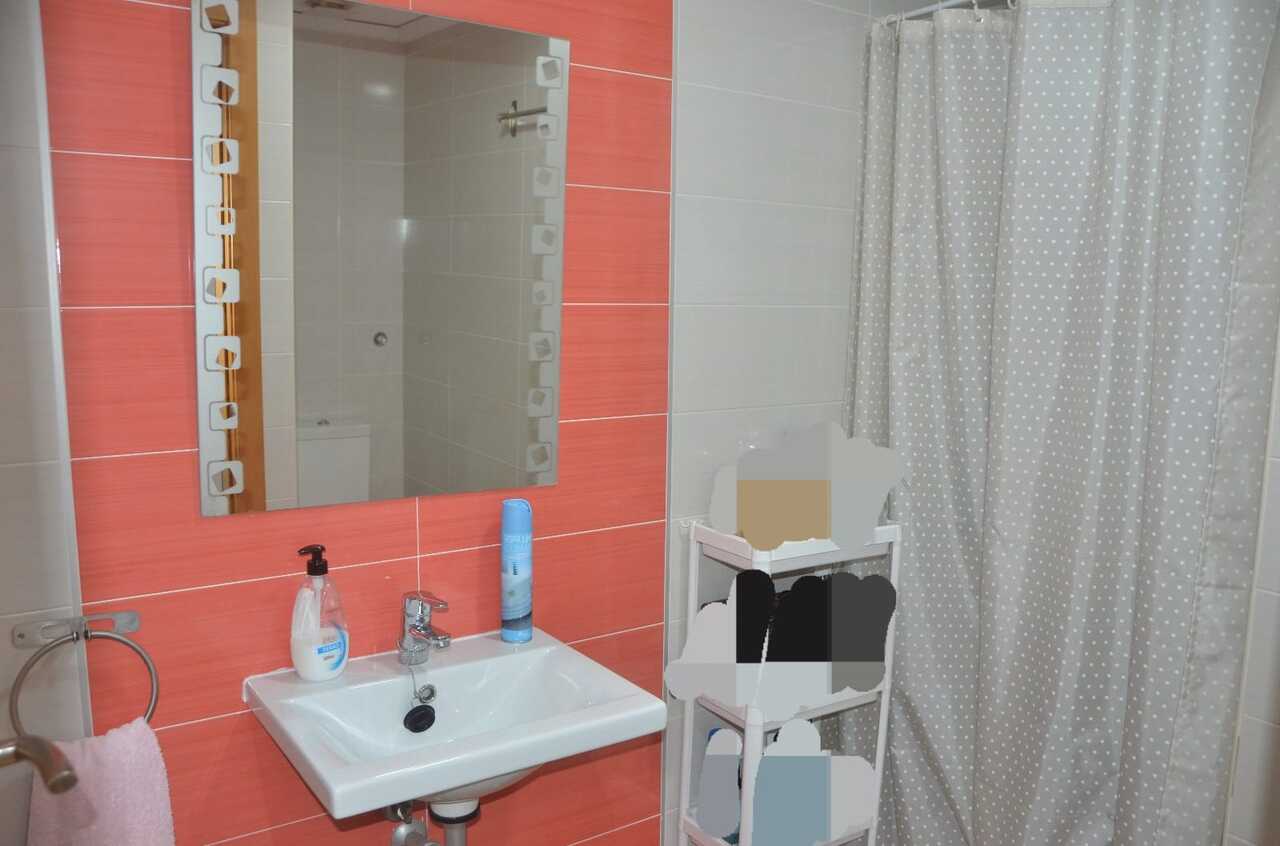 Salle de bain avec carrelage mural corail, lavabo en céramique blanche et miroir décoratif à côté d'un rideau de douche à pois.
