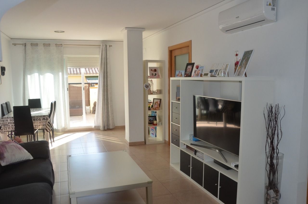 Salon-salle à manger lumineux avec sol en grès cérame, meuble TV modulaire, climatisation murale et accès direct à une terrasse extérieure.