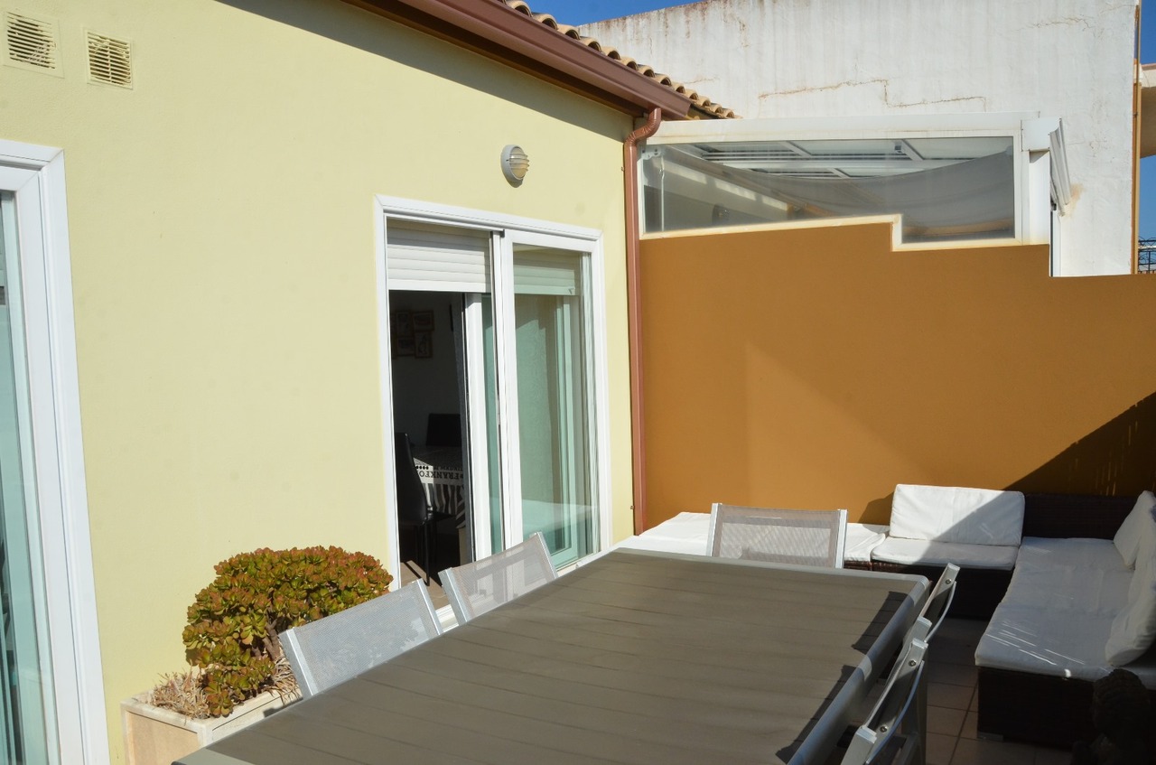Terrasse privée avec table à manger extérieure, chaises en maille et espace lounge avec coussins blancs bordé d'un mur de protection ocre.