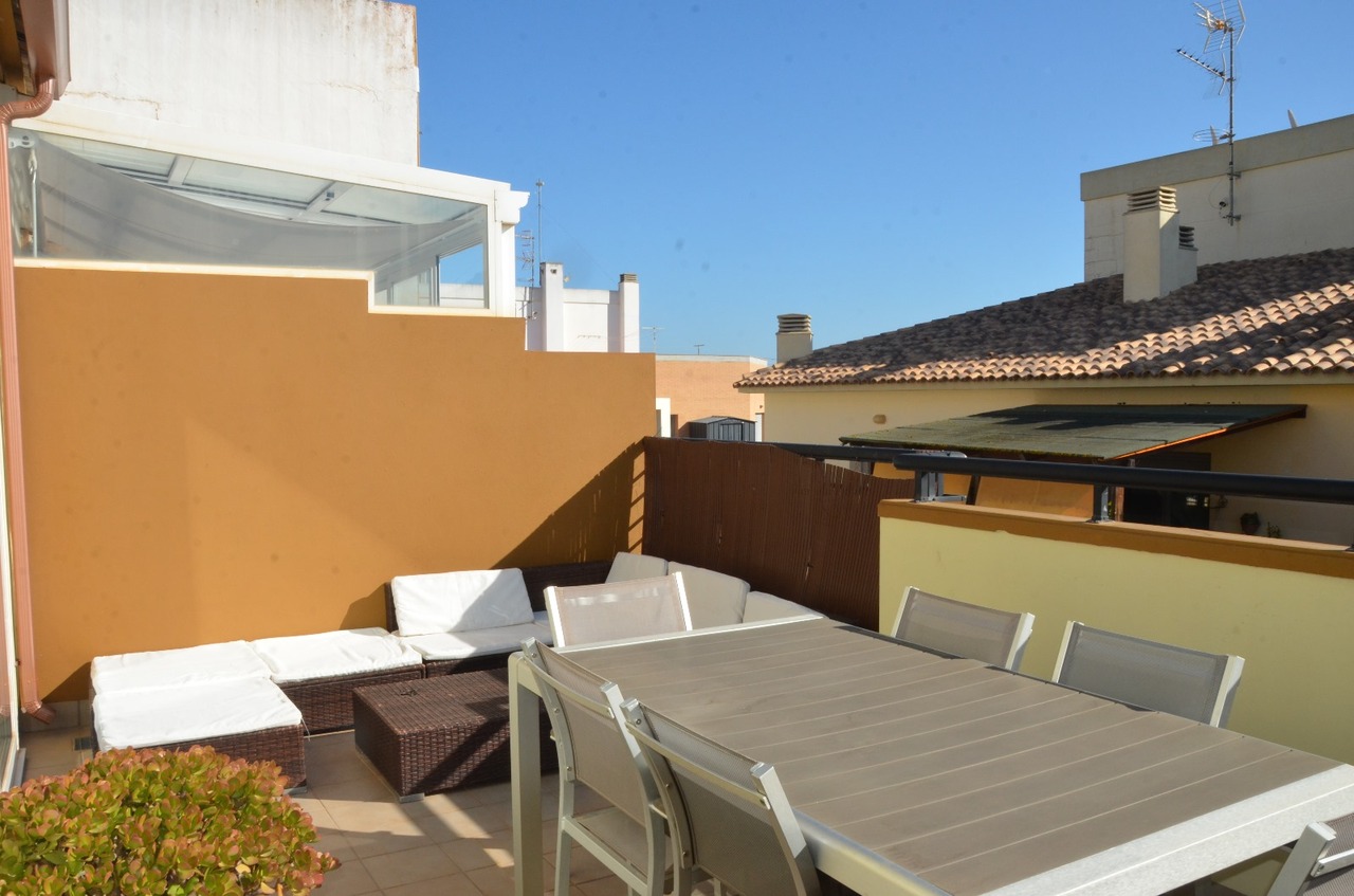Terrasse sur le toit avec un ensemble de salle à manger gris et un salon en rotin aux coussins blancs, offrant une vue dégagée sur les toits.