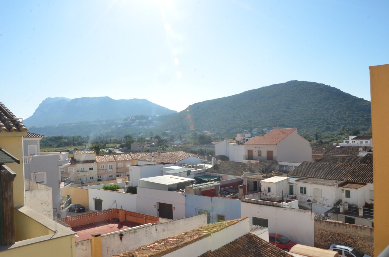 Vue panoramique surélevée sur les toits traditionnels du village et les montagnes verdoyantes en arrière-plan sous un ciel clair.