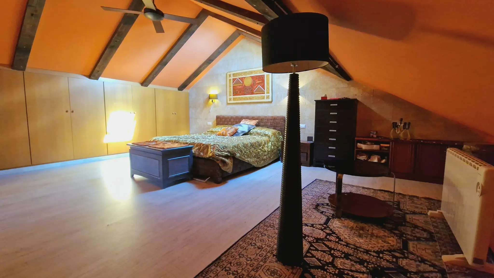 Chambre mansardée avec poutres apparentes en bois sombre, placards intégrés en bois clair et mur d'accent en pierre naturelle sous le toit incliné.