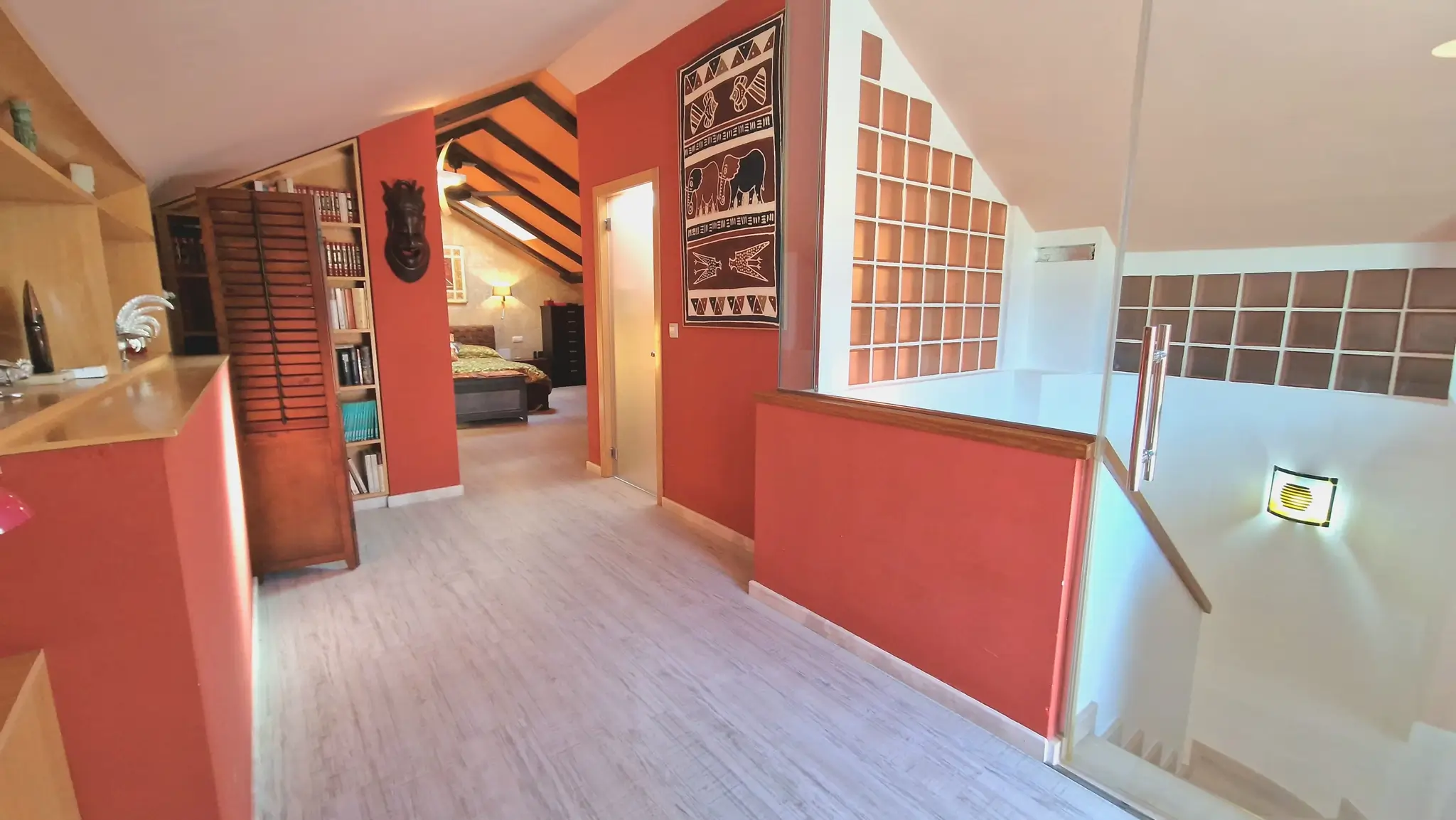 Palier avec murs terracotta, sol en bois clair et garde-corps vitré. L'espace s'ouvre sur une chambre mansardée aux poutres apparentes et rangements intégrés sur mesure.