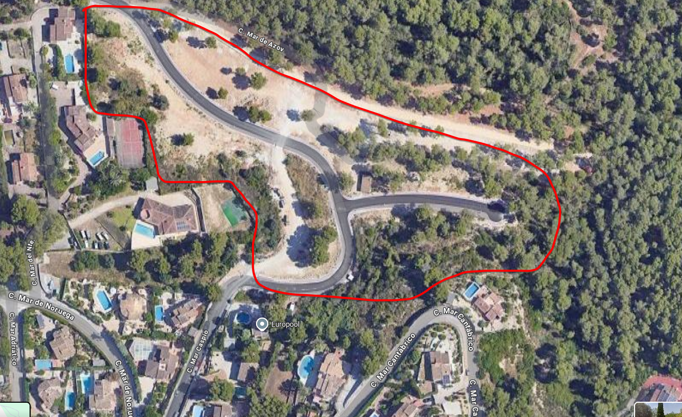 Vue aérienne d'un terrain constructible délimité en rouge, incluant des voies d'accès goudronnées et une végétation méditerranéenne à proximité de villas.