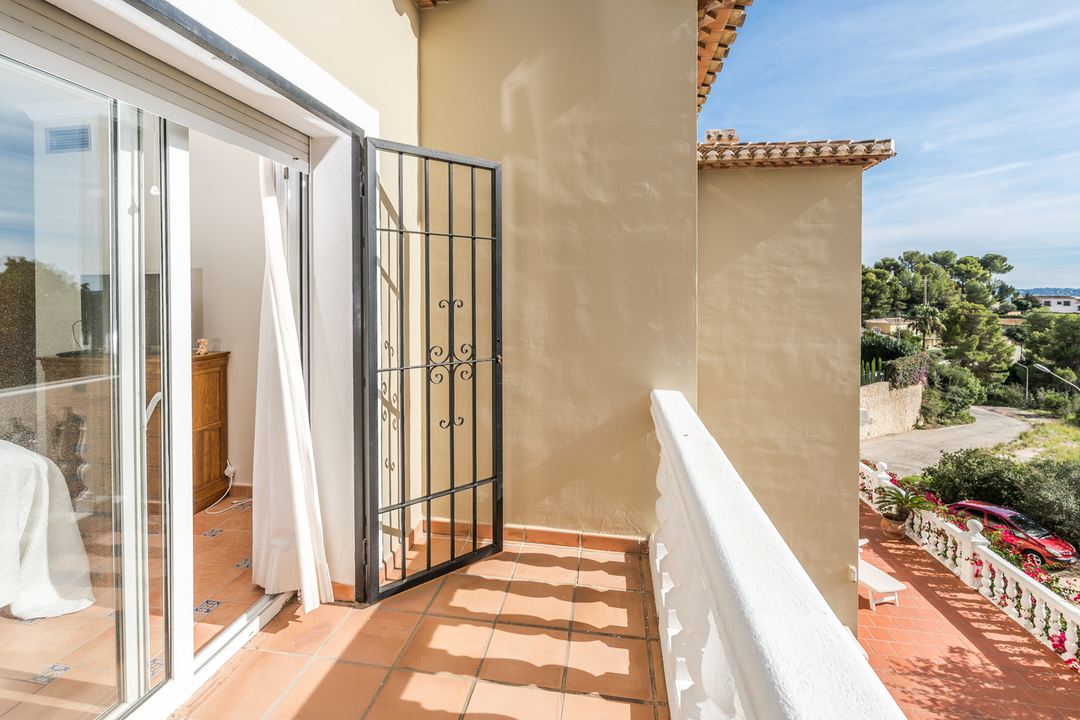 Balcon privé avec carrelage en terre cuite et balustrade blanche, doté d'une grille de sécurité en fer forgé et vue sur le paysage méditerranéen.