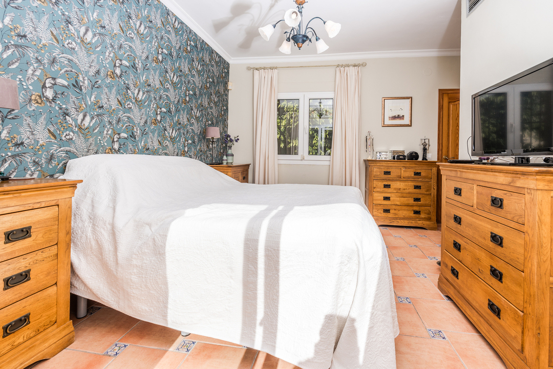 Chambre à coucher avec papier peint tropical, commodes en bois assorties et sol en terre cuite orné de carreaux décoratifs.