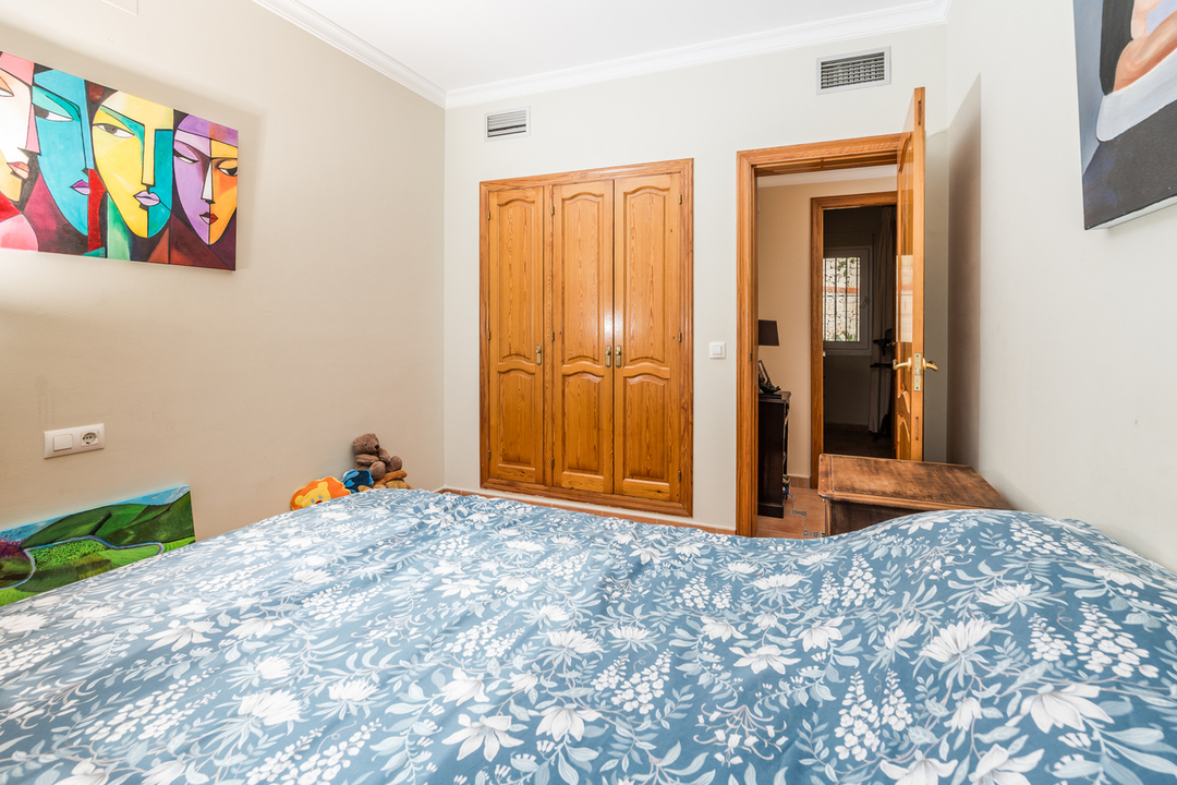 Chambre avec armoire encastrée en bois, murs clairs décorés d'art moderne et lit avec linge de maison aux motifs floraux bleus.