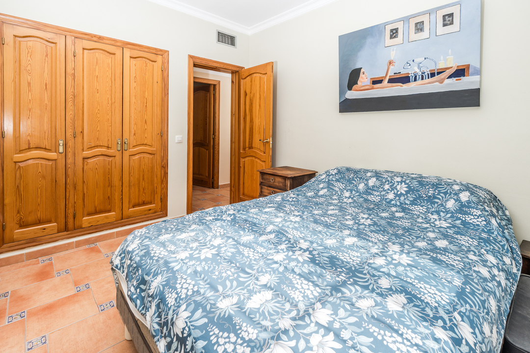 Chambre avec armoire encastrée en bois naturel, sol en terre cuite avec inserts décoratifs et lit double aux motifs floraux.
