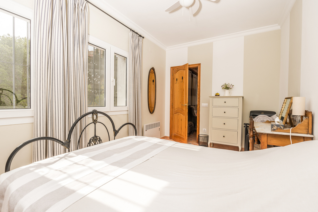 Chambre avec tête de lit en fer forgé, bureau en bois classique et fenêtres avec rideaux à rayures offrant une lumière naturelle abondante.