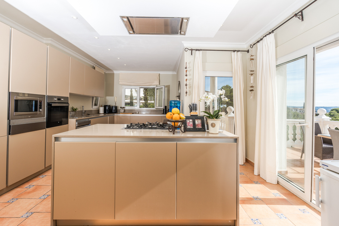 Cuisine contemporaine avec îlot central, électroménager encastré et sol en terre cuite. Les baies vitrées offrent une lumière naturelle et un accès extérieur.