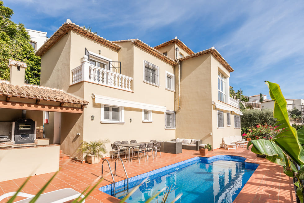 Façade de villa méditerranéenne avec piscine, terrasse en terre cuite, coin repas extérieur et cuisine d'été sous un auvent traditionnel.
