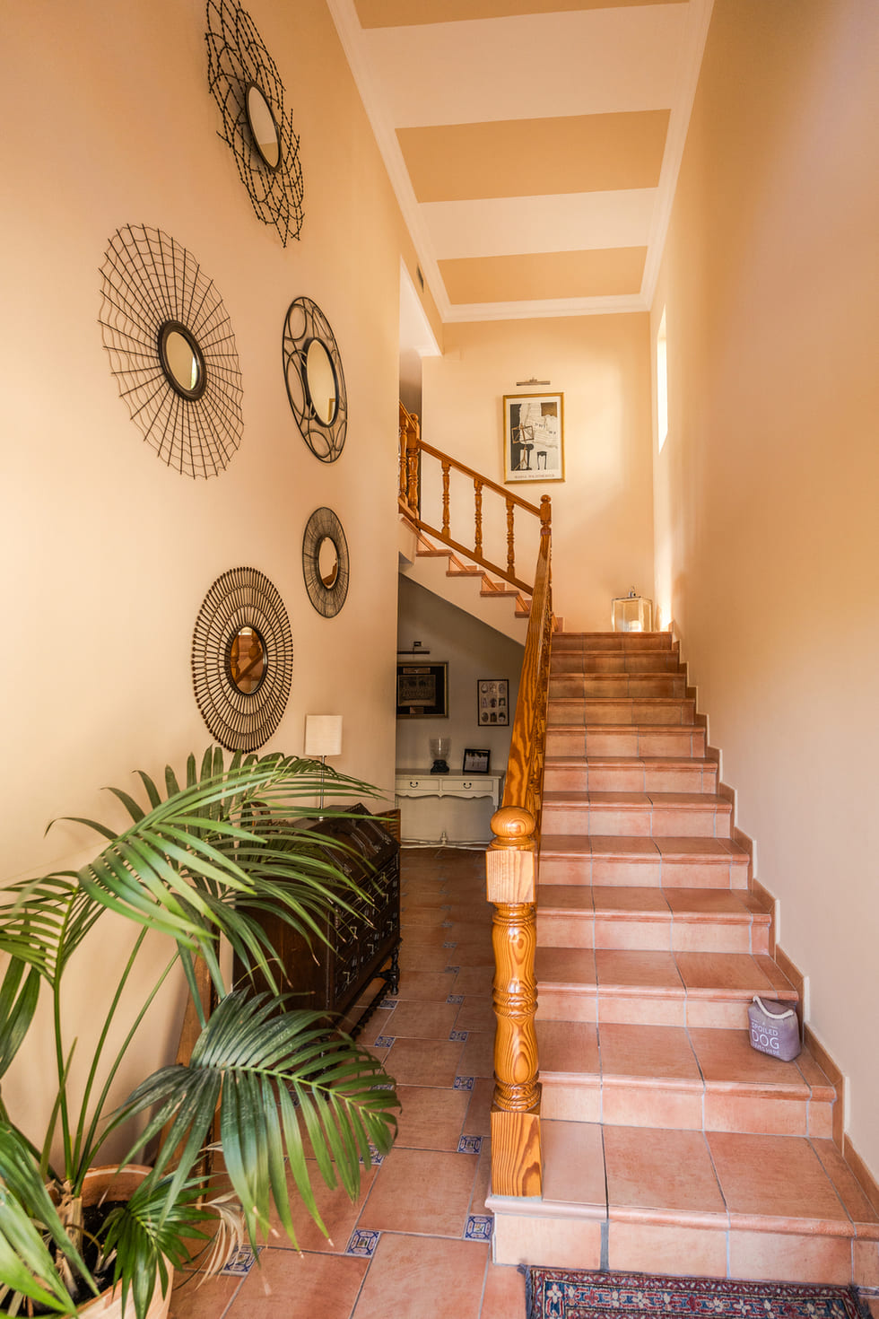 Hall d'entrée avec escalier en terre cuite, rampe en bois, miroirs décoratifs en métal et plafond à rayures élégantes.