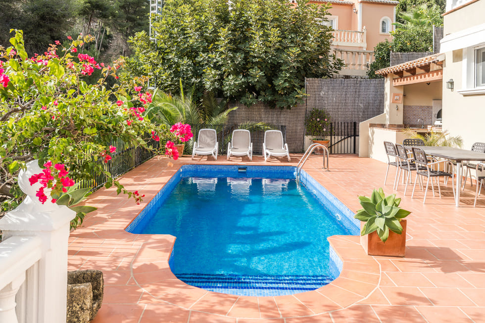 Piscine rectangulaire en mosaïque bleue entourée d'une terrasse en terre cuite, avec chaises longues, espace repas extérieur et bougainvilliers en fleurs.
