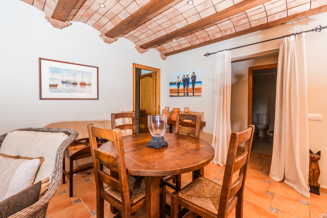 Salle à manger avec plafond voûté en briques et poutres en bois, sol en terre cuite et mobilier rustique incluant une table ronde et des chaises en paille.