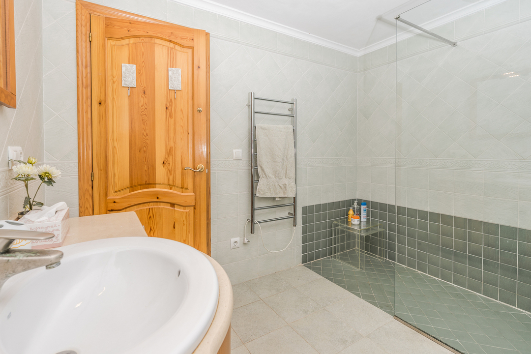 Salle de bain avec douche à l'italienne, carrelage vert, paroi vitrée et sèche-serviettes chromé à côté d'une porte en bois massif.