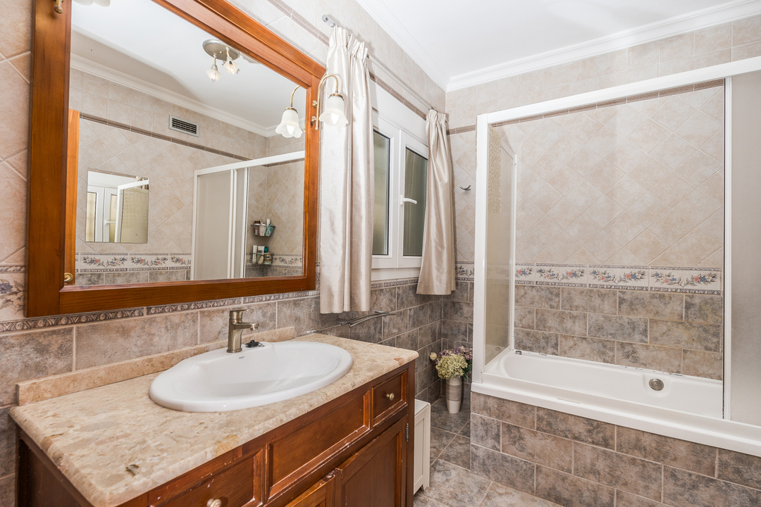 Salle de bain avec meuble en bois sous vasque en marbre, grand miroir encadré et baignoire équipée d'une paroi coulissante sur un carrelage mural décoratif.