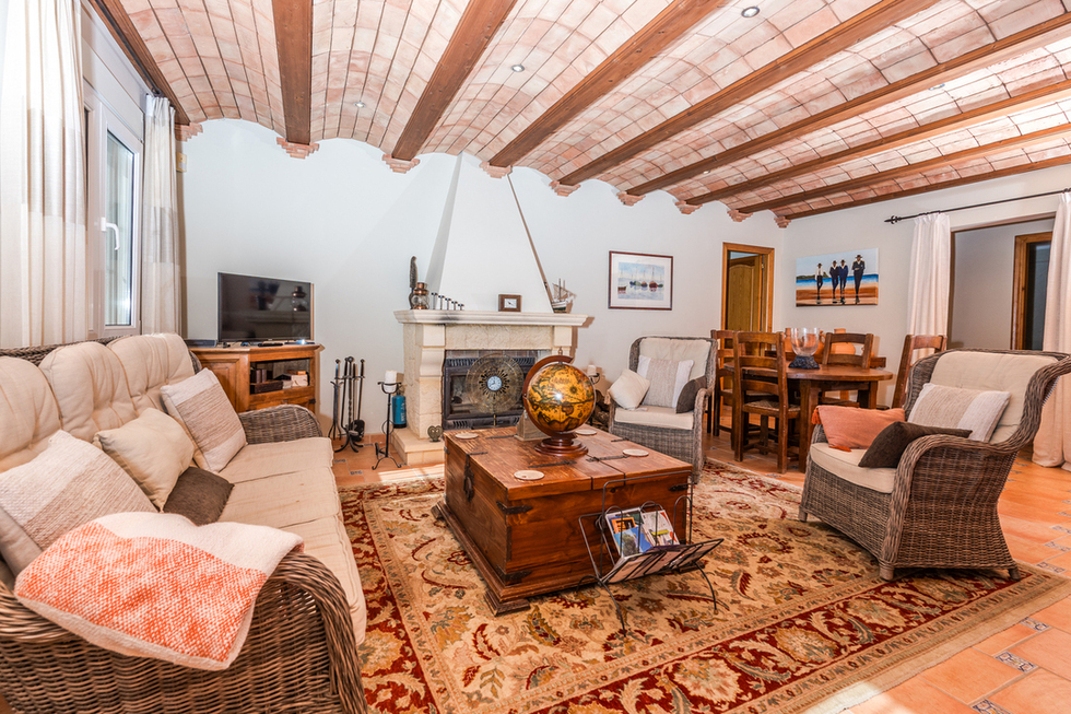 Salon avec plafond en voûte catalane et poutres en bois, cheminée en pierre et mobilier en osier sur un sol en terre cuite traditionnelle.