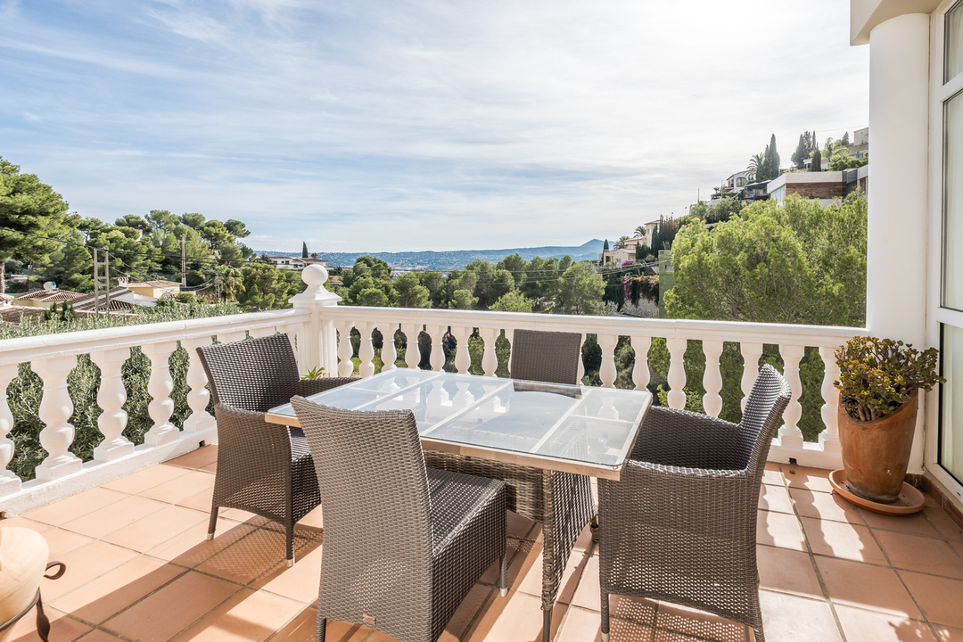 Terrasse avec carrelage en terre cuite et balustrade blanche, dotée d'un coin repas en rotin offrant une vue panoramique sur la vallée.