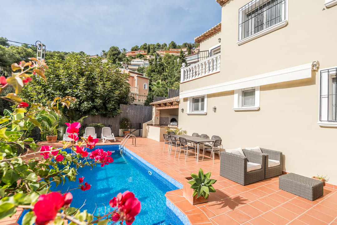 Terrasse avec piscine privée, revêtement en terre cuite et coin repas extérieur. Comprend un barbecue intégré et du mobilier de salon devant une façade crème.