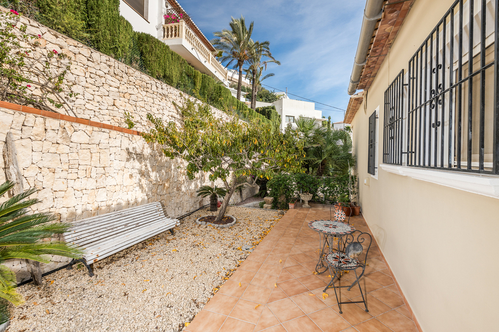Terrasse latérale avec carrelage en terre cuite, espace gravillonné avec banc blanc et mur de soutènement en pierre naturelle.
