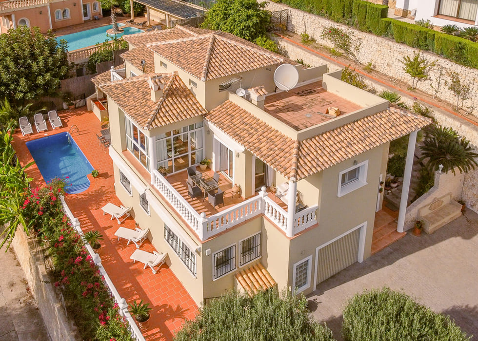 Vue aérienne d'une villa méditerranéenne avec toits en terre cuite, piscine privée et terrasses à balustrades blanches incluant un espace dînatoire.