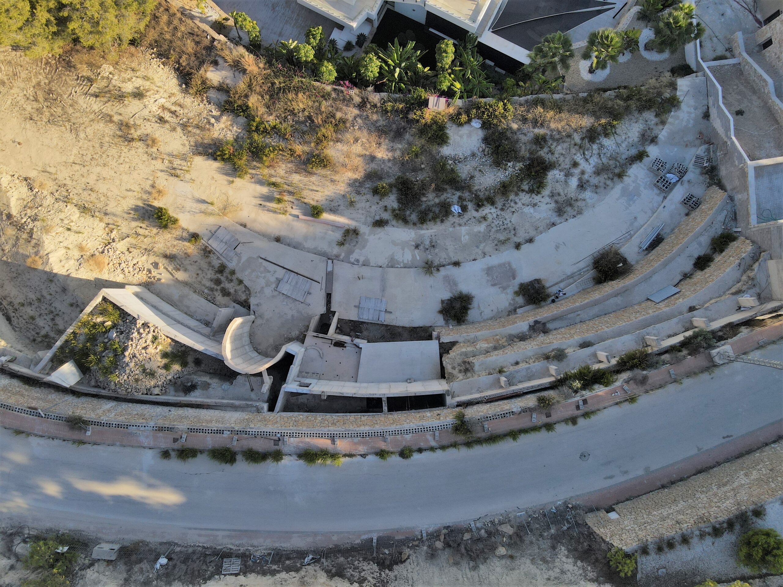 Vue aérienne d'un terrain en construction avec des fondations en béton courbes et des murs de soutènement en pierre sur un terrain en pente.