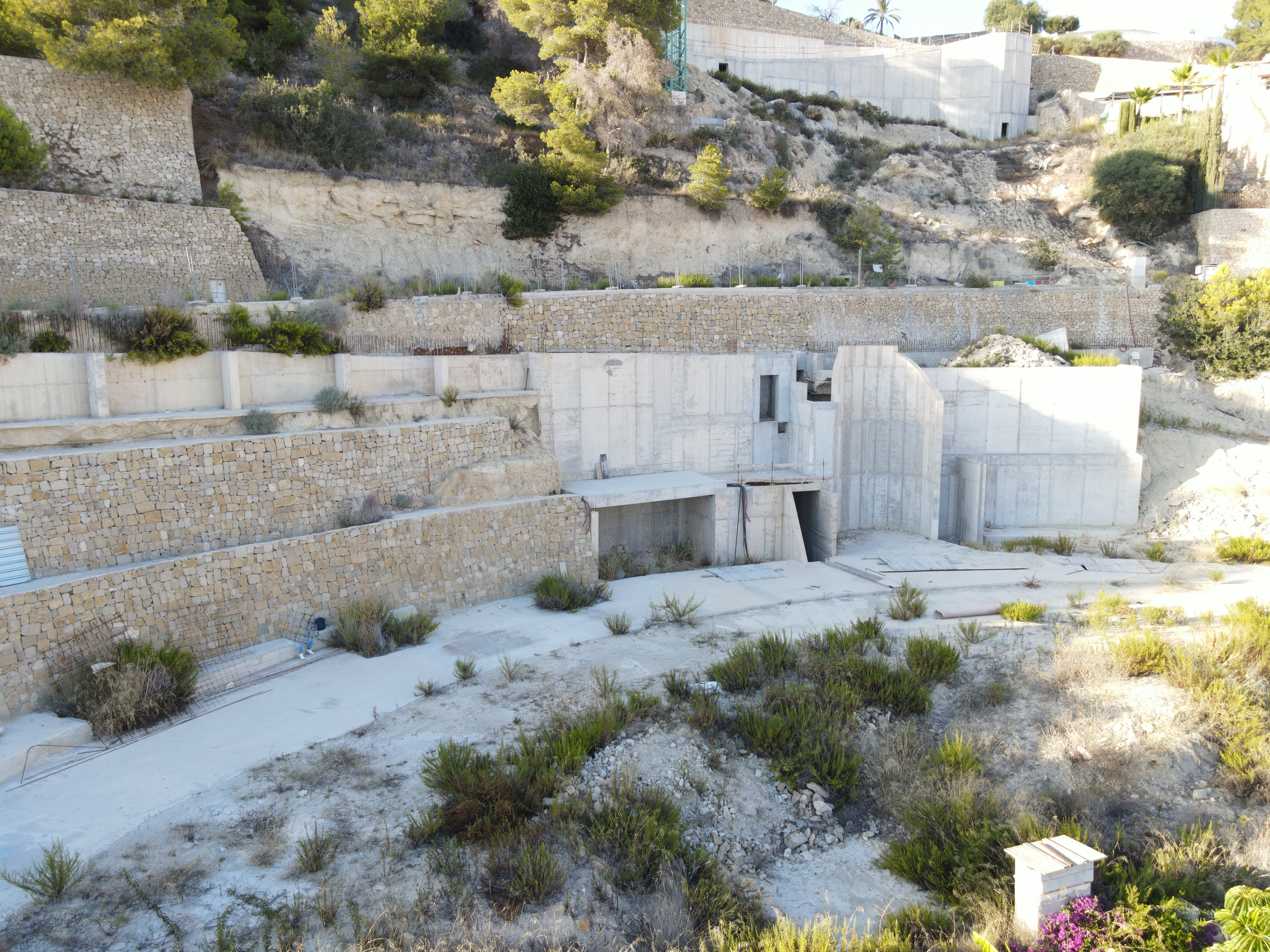 Vue du chantier présentant des murs de soutènement en pierre sèche et des structures en béton armé intégrées à la colline.