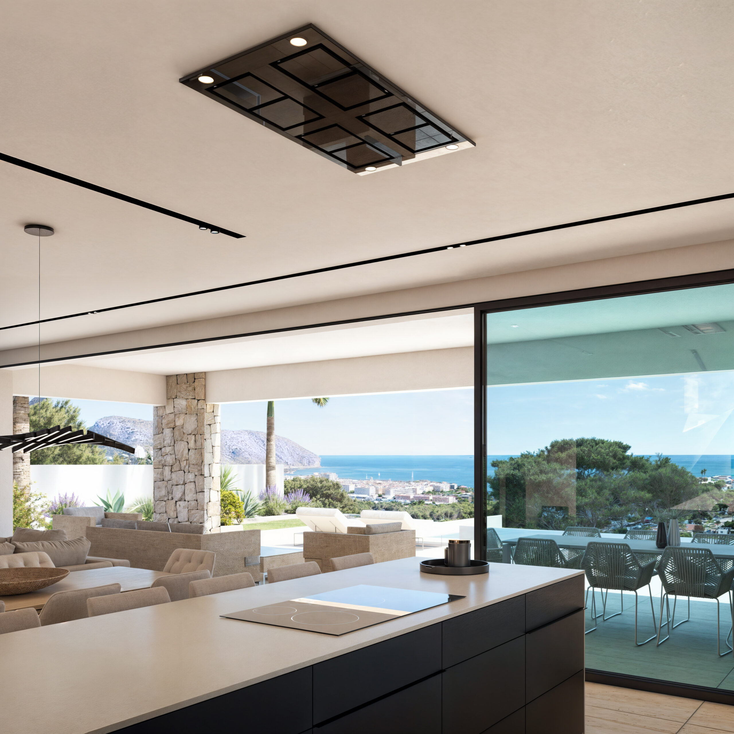 Îlot de cuisine avec plaque à induction et hotte de plafond, s'ouvrant sur un salon lumineux et une terrasse avec vue sur la côte.