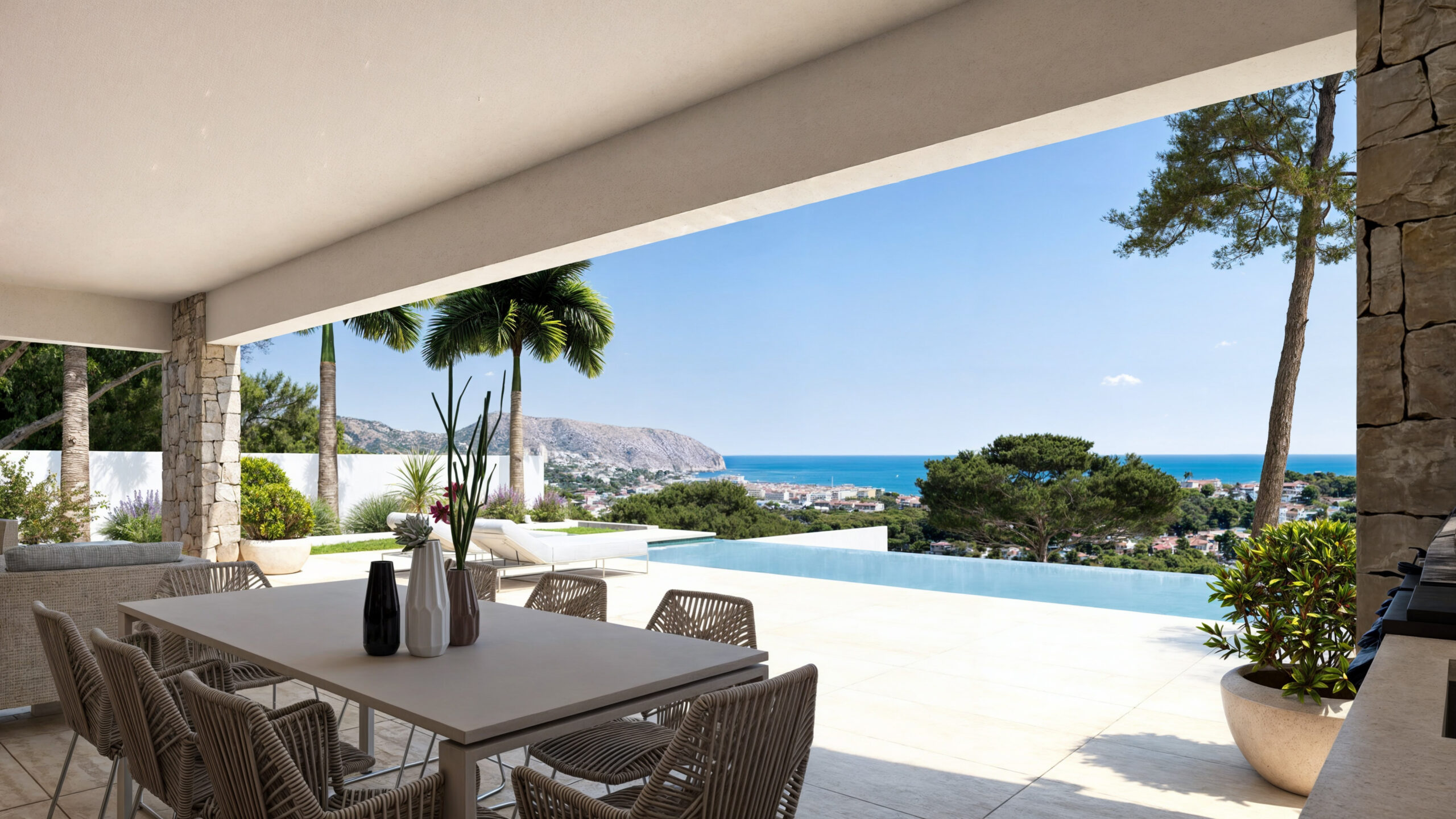Terrasse couverte avec espace repas, piliers en pierre et piscine à débordement offrant une vue panoramique sur la mer et les montagnes environnantes.
