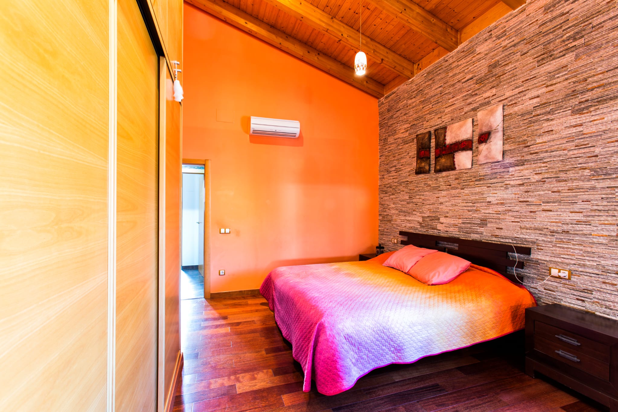 Chambre avec plafond rampant en bois, mur de parement en pierre et placards intégrés. L'espace dispose d'un sol en parquet et d'un système de climatisation individuel.
