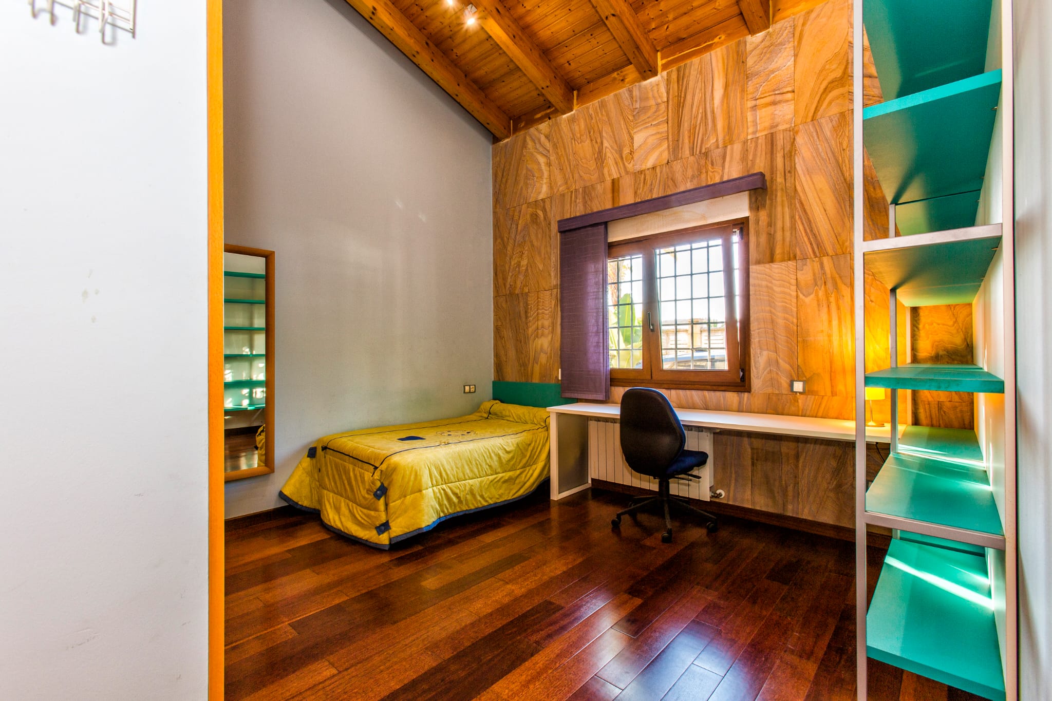 Chambre individuelle avec plafond voûté en bois, mur d'accent en pierre texturée, bureau intégré et parquet en bois sombre élégant.