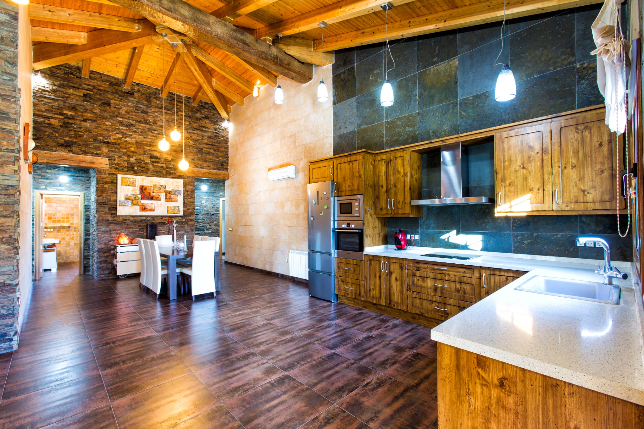 Cuisine ouverte et salle à manger avec plafond voûté en bois, murs en pierre naturelle, armoires rustiques et appareils en acier inoxydable.