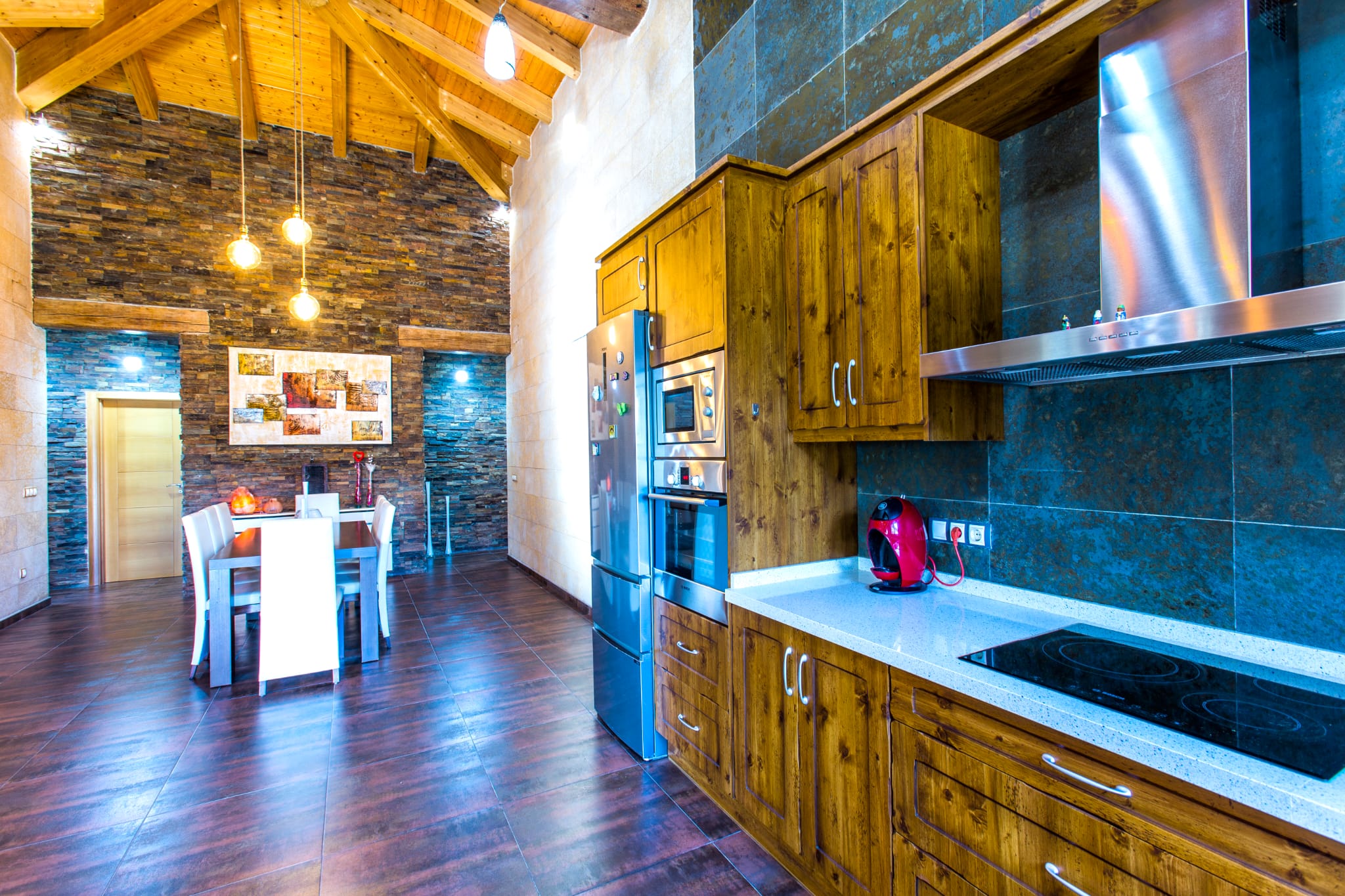 Cuisine rustique avec meubles en bois, électroménager encastré et plafond voûté en bois. Un mur en pierre apparente apporte du caractère à l'espace salle à manger.