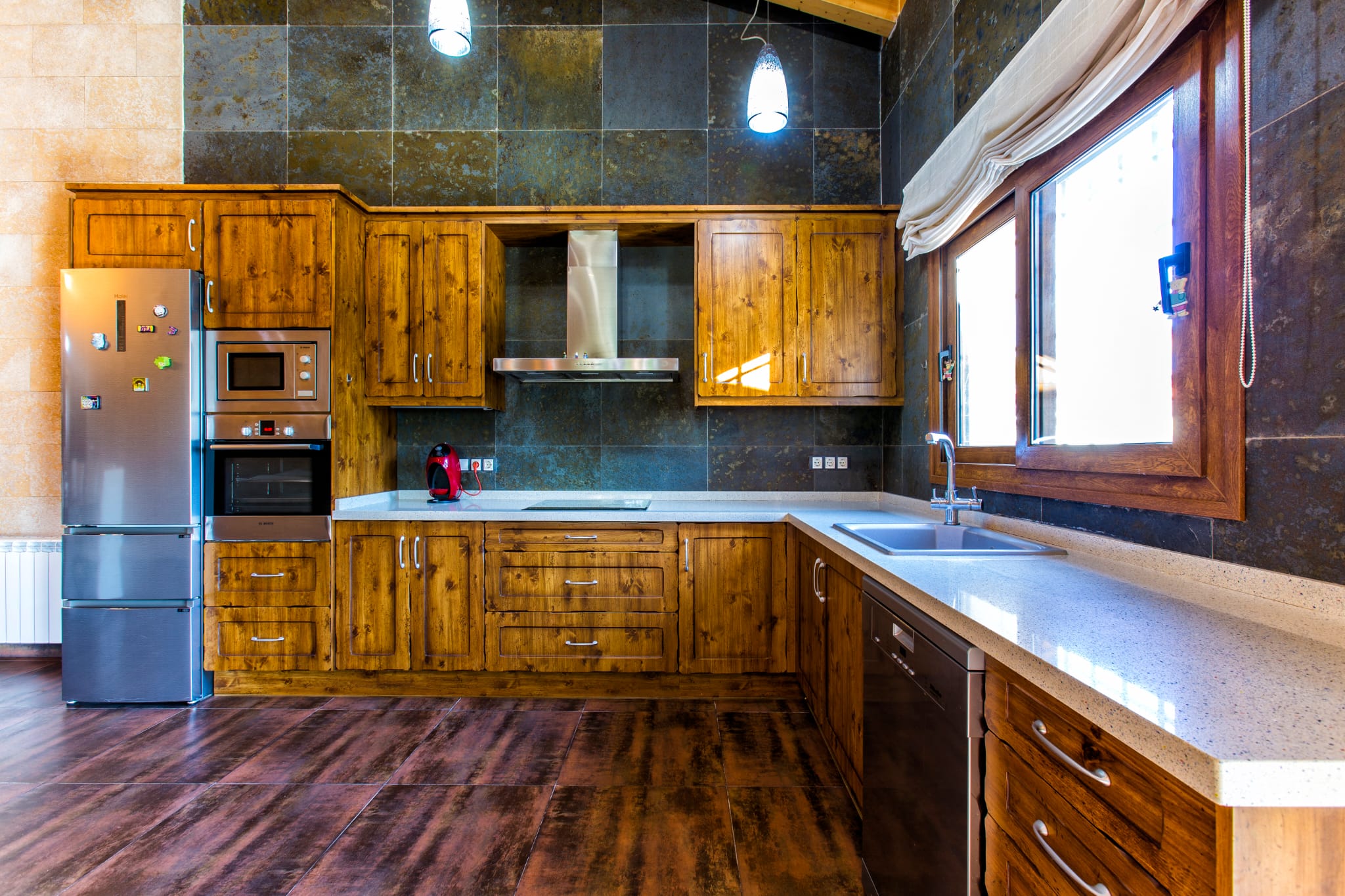 Cuisine rustique avec placards en bois massif, murs en pierre sombre et plan de travail en quartz clair, dotée d'appareils encastrés en acier inoxydable.