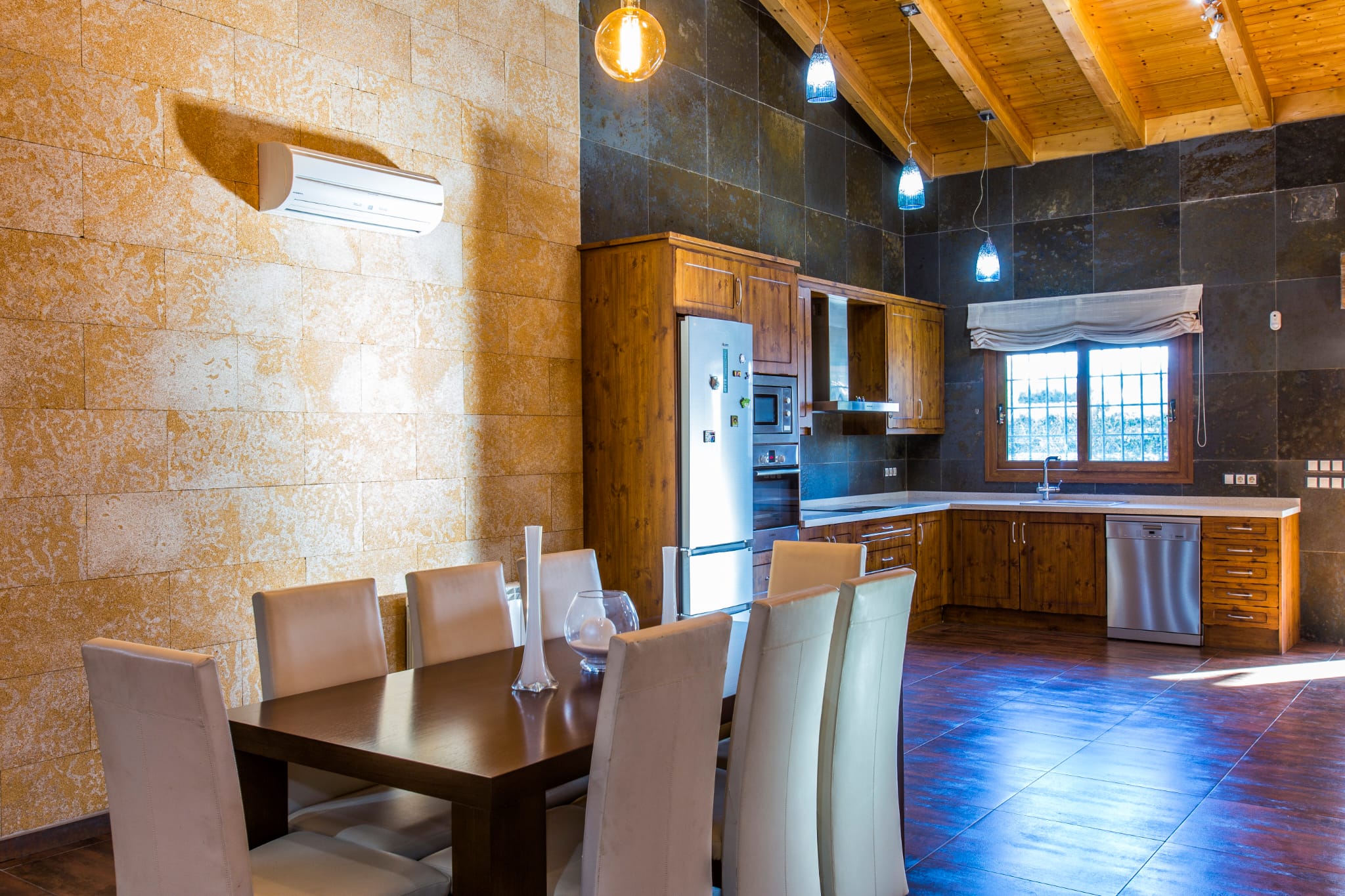 Espace cuisine et salle à manger avec plafond voûté en bois, murs en pierre texturée, meubles rustiques et appareils électroménagers en acier inoxydable.