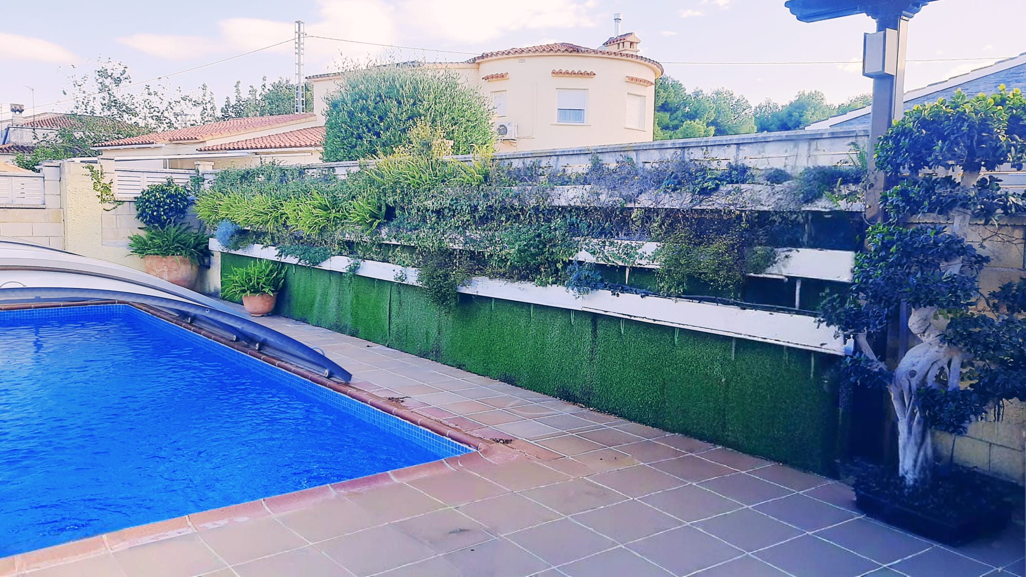 Espace piscine extérieure avec terrasse carrelée, abri télescopique et mur végétal à plusieurs niveaux sur une base de gazon synthétique.
