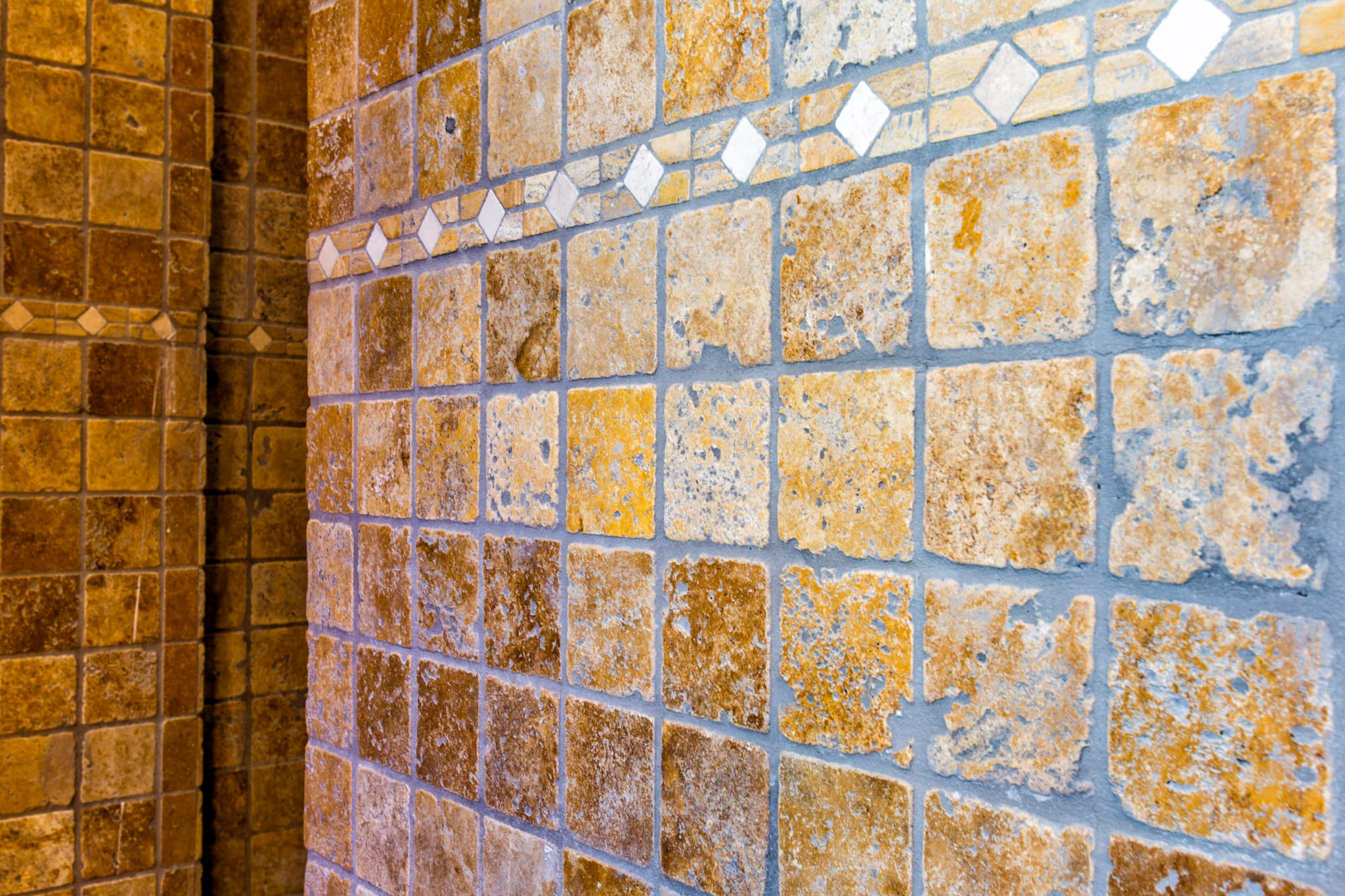 Gros plan sur des carreaux en pierre naturelle ocre à la texture rustique, soulignés par une frise décorative à motifs losanges.