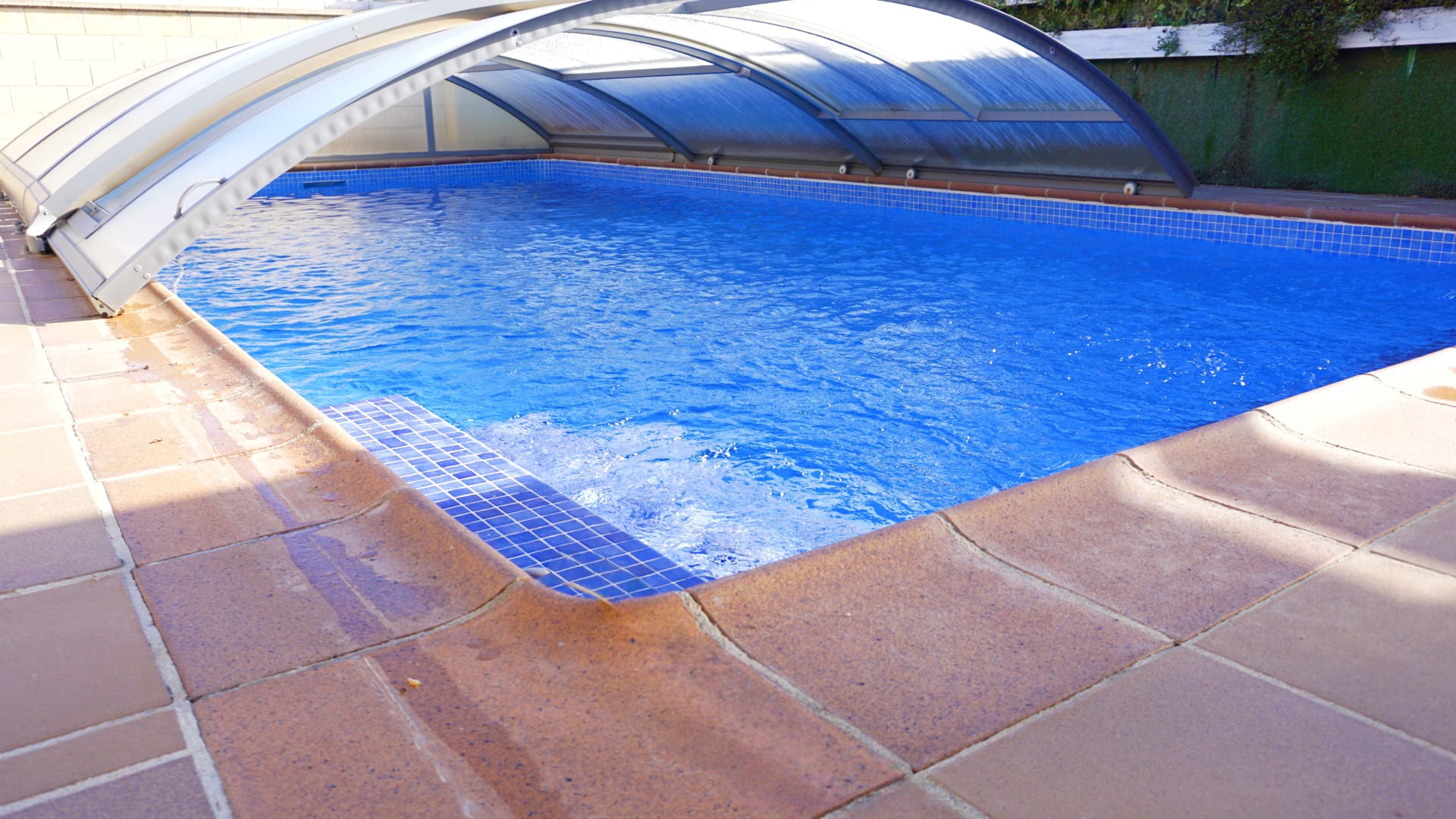 Piscine extérieure équipée d'un abri télescopique, revêtement en mosaïque bleue et plage en dalles de pierre naturelle.