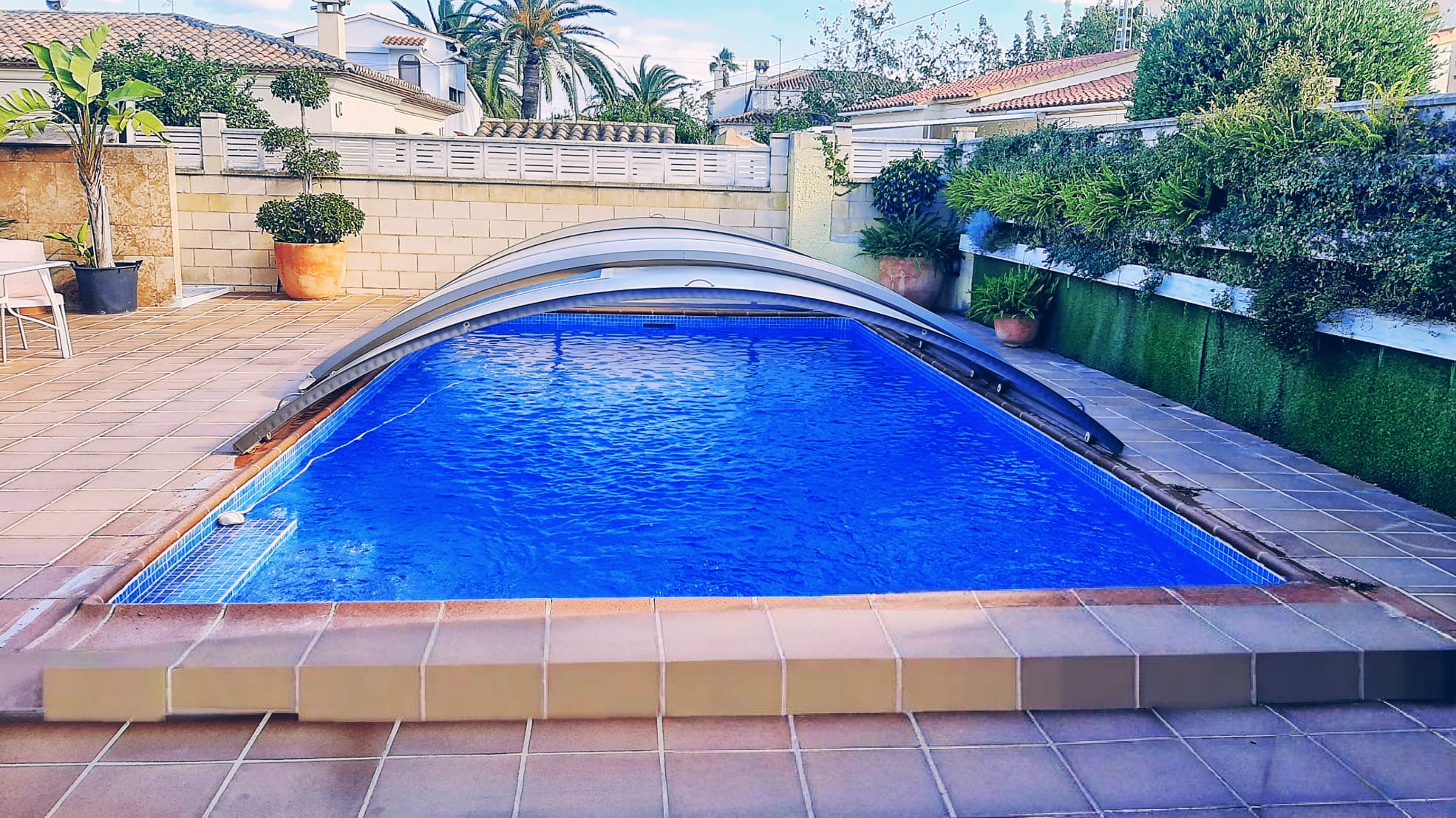 Piscine privée avec abri télescopique et revêtement en mosaïque bleue, entourée d'une terrasse en grès et de murs végétalisés.
