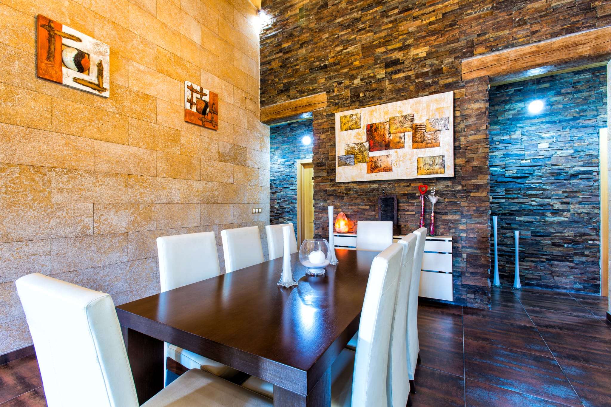Salle à manger avec table en bois foncé et chaises blanches, entourée de murs en pierre naturelle et ardoise texturée.