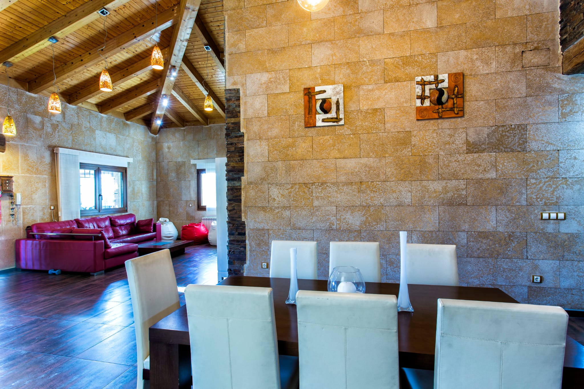 Salle à manger ouverte avec murs en pierre, plafond voûté en bois aux poutres apparentes et mobilier contemporain contrastant avec les matériaux rustiques.
