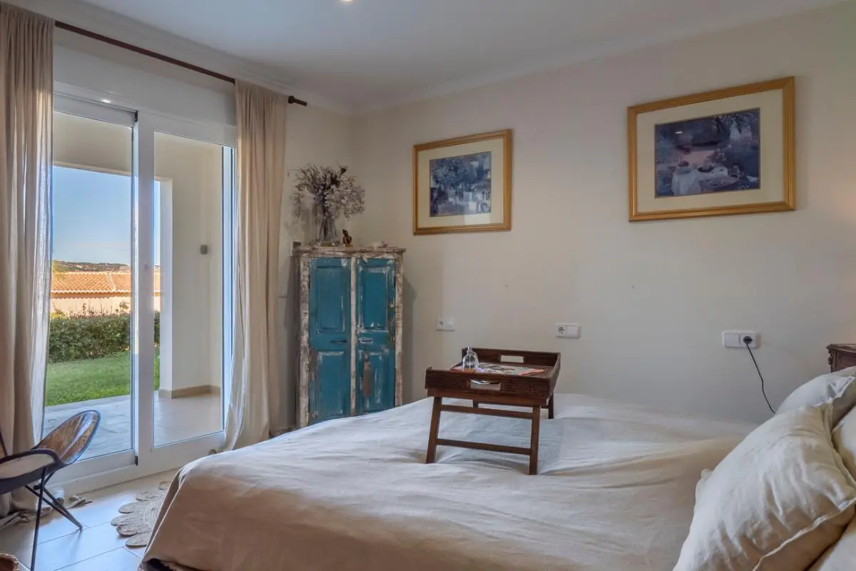 Chambre avec accès direct à la terrasse, armoire rustique en bois bleu et grandes baies vitrées offrant une vue dégagée sur le jardin et la pelouse.