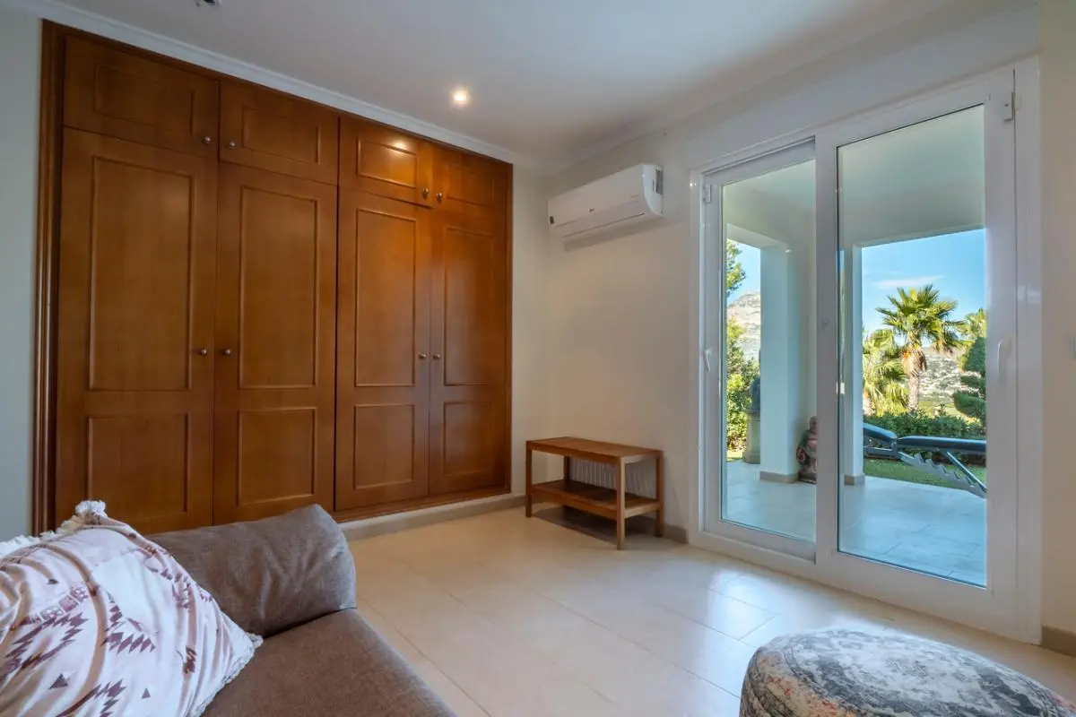 Chambre équipée d'un grand placard intégré en bois, d'une climatisation et de baies vitrées coulissantes ouvrant sur une terrasse et le jardin.
