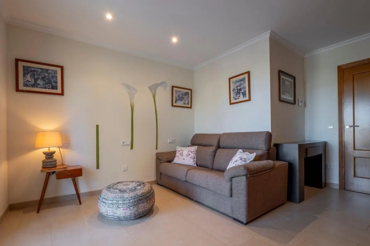 Coin salon avec un canapé en tissu marron, un pouf à motifs et une table d'appoint. Décoration murale avec des fleurs, des cadres et des spots encastrés.