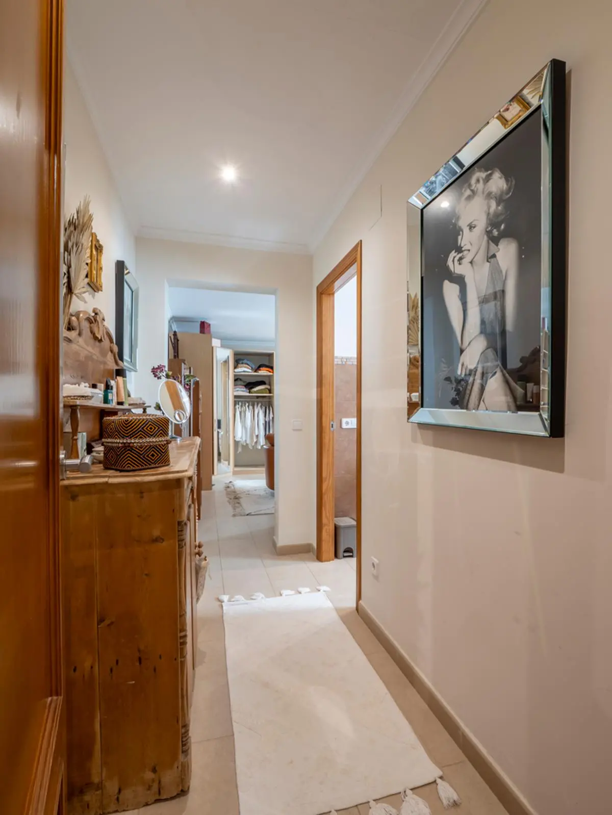 Couloir lumineux avec une commode en bois rustique, un portrait encadré de miroirs et une vue sur un dressing aménagé avec étagères et penderies.