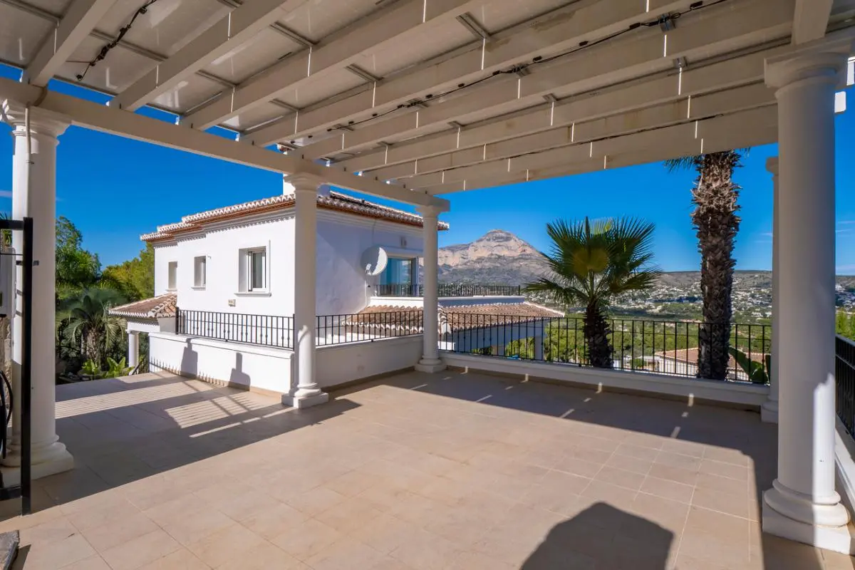 Grande terrasse couverte avec colonnes blanches et pergola, offrant une vue panoramique sur le mont Montgó et la vallée environnante.