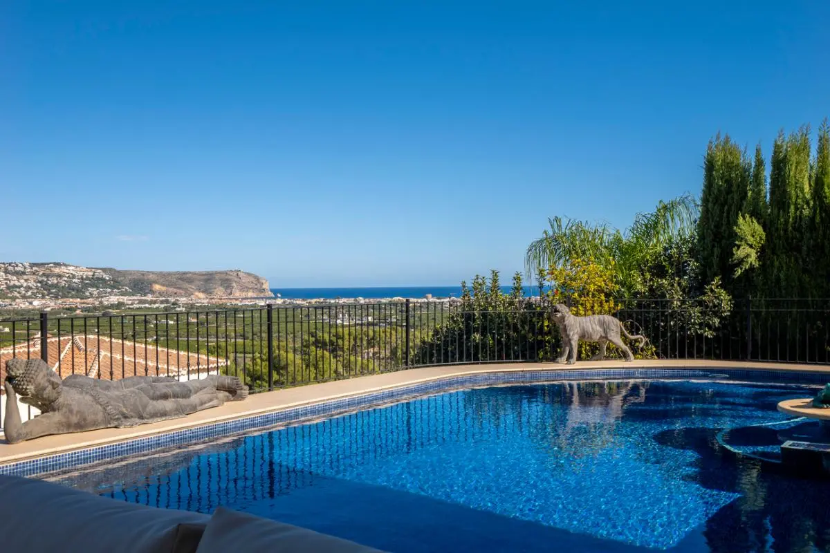 Piscine extérieure avec mosaïque bleue, statues décoratives en pierre et vue panoramique sur la mer Méditerranée et le paysage côtier.