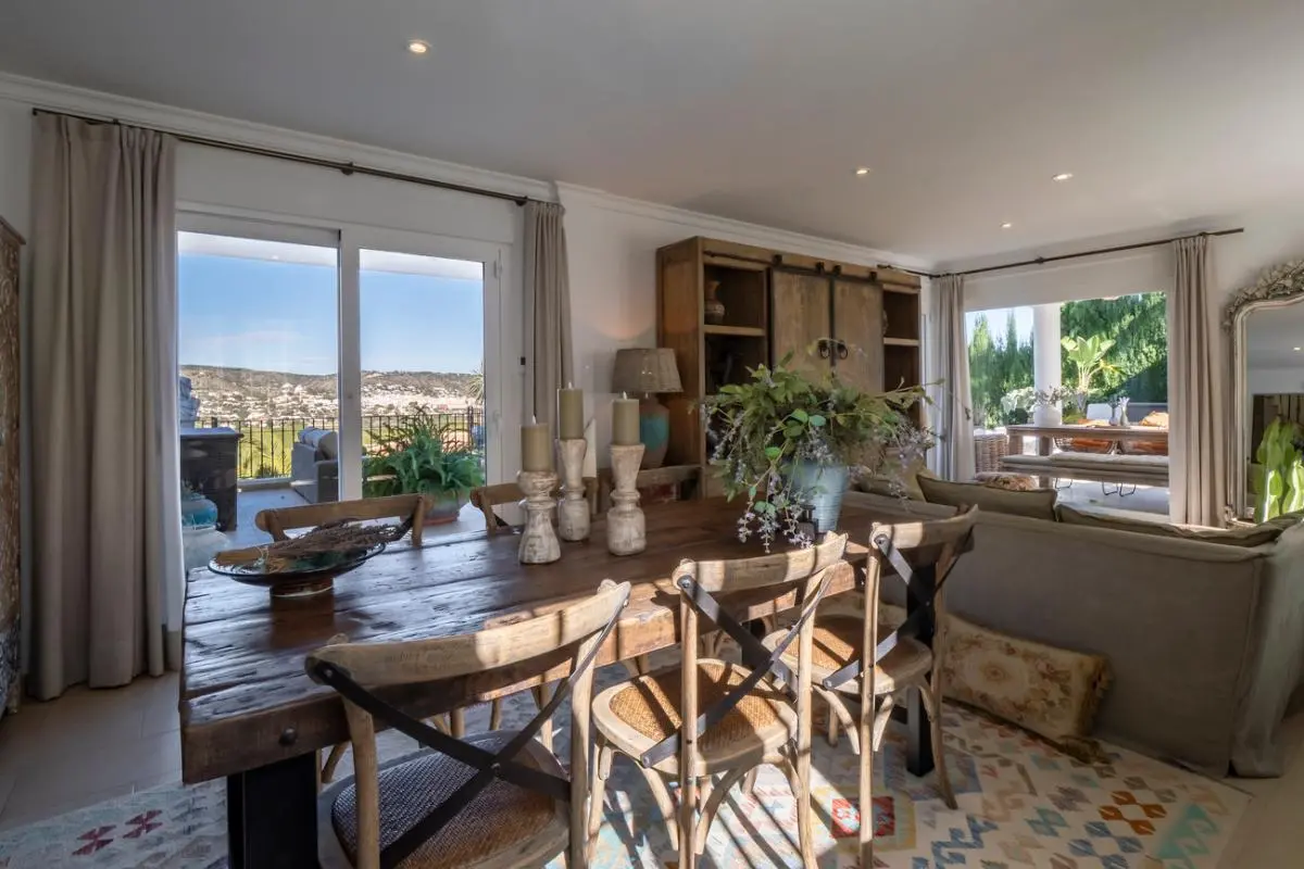 Salle à manger rustique avec table en bois massif et chaises à dossier croisé, offrant un accès direct à une terrasse avec vue sur la vallée.