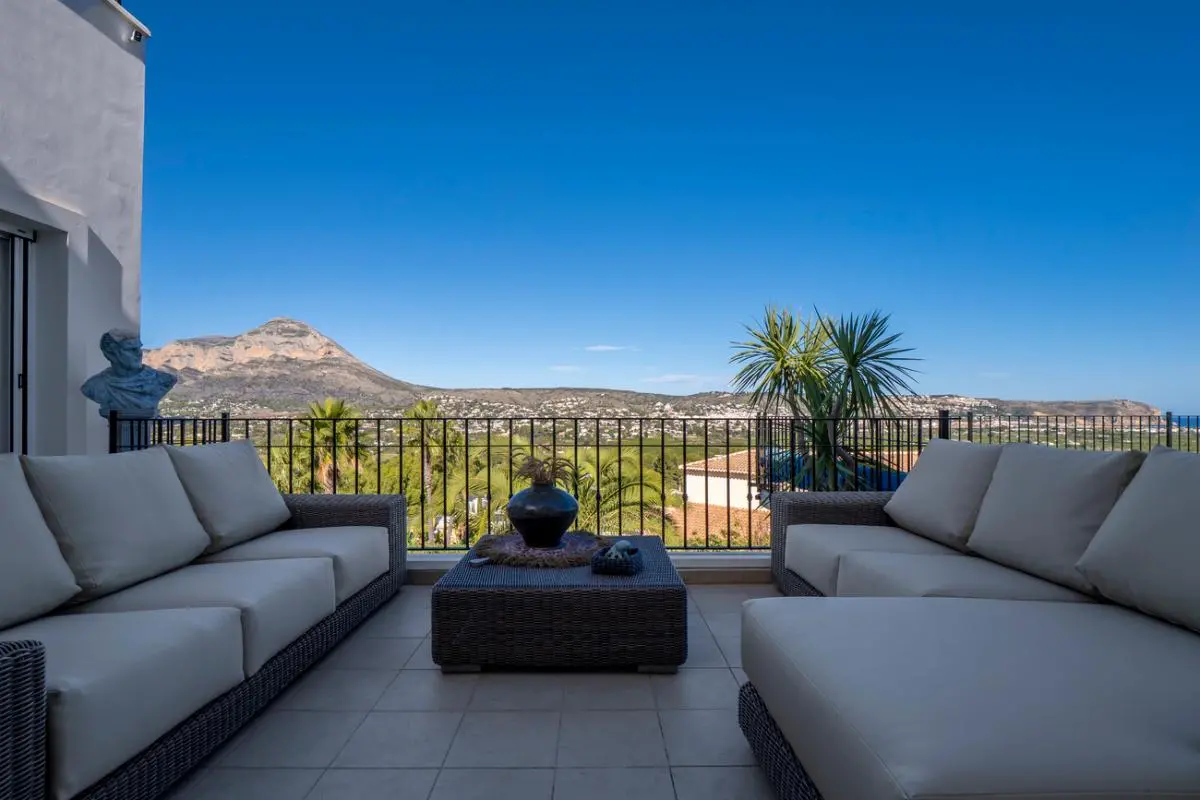 Salon de terrasse avec mobilier en osier gris offrant une vue panoramique sur le mont Montgó et la vallée environnante.